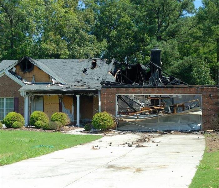A picture of a home that has experienced a house fire. Part of the roof has collapsed. Burnt marks can be seen on the home.