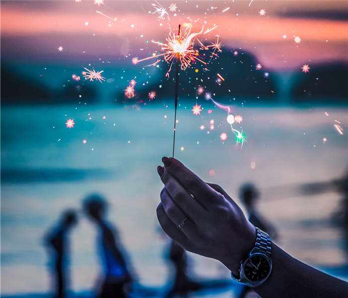 sparkler in a hand with people in the background with a pinkish sky