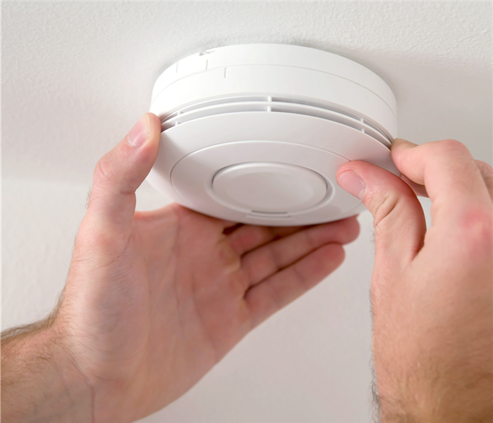 two hands around a smoke alarm on the ceiling 